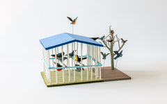 Vogelhaus: Bemalte Holzarbeit, Sicht von oben auf das hellblaue Dach des Vogelhauses mit weissen Gitterstäben.