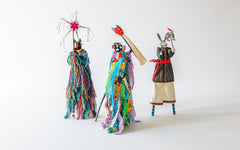 Karneval Tier-Figuren auf Stelzen in farbenfrohen Gewändern, Attribute auf Stäben tragend.