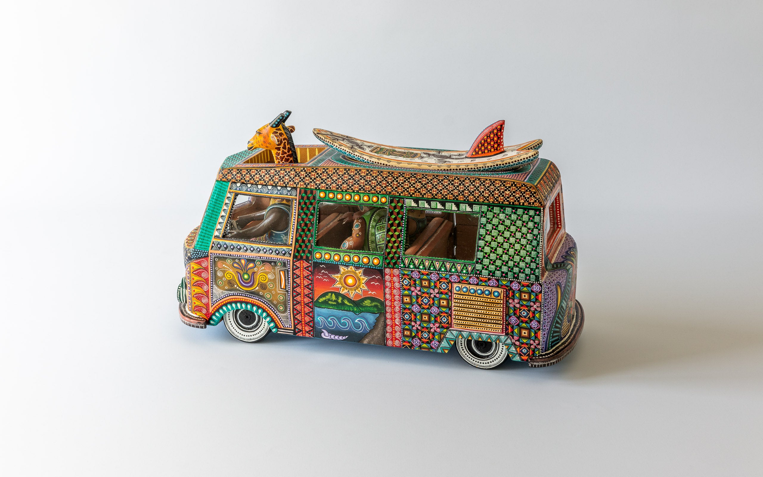 VW Kombi Surfen: Sicht auf die eine Seite des farbig bemalten VW Kombi mit Giraffe am Steuer und Surfboard auf Dach.